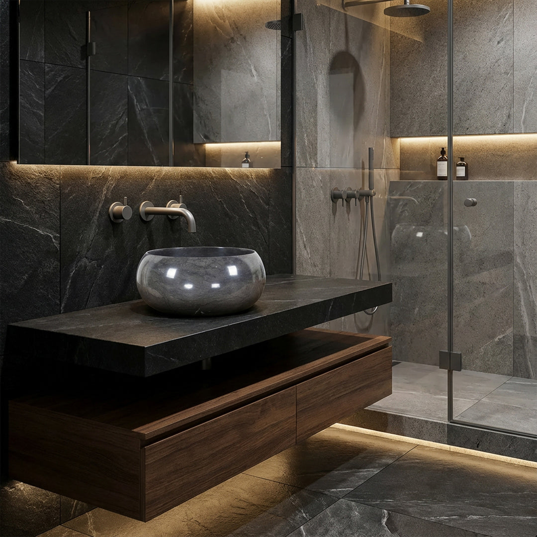 Rundes Aufsatzwaschbecken aus Naturstein auf dunklem Waschtisch im modernen Spa-Badezimmer, kombiniert mit Wandarmatur, Glasdusche und indirekter Beleuchtung