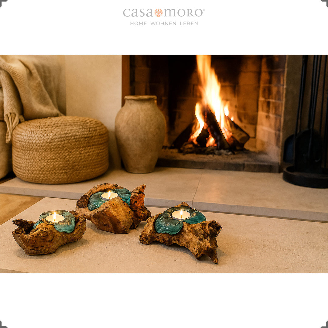 Drei Teelichthalter aus Glas und Wurzelholz vor einem brennenden Kamin, ihr sanftes Licht unterstreicht die gemütliche Wohnatmosphäre.