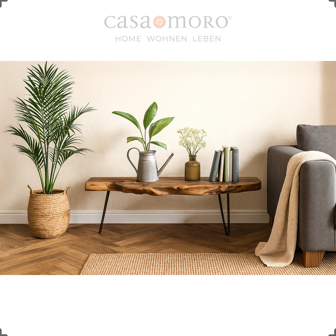  Holz-Tisch aus Teak im Wohnzimmer-Ambiente mit Pflanzendeko, Teppich und Sofa