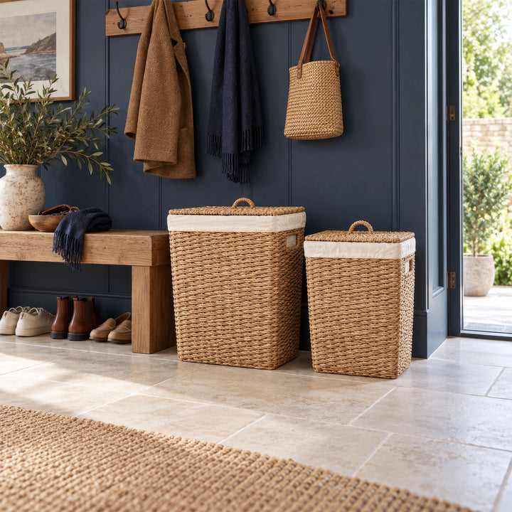 Due cesti in erba marina con coperchi chiusi vicino a panca in legno nell’ingresso con pareti blu scuro.