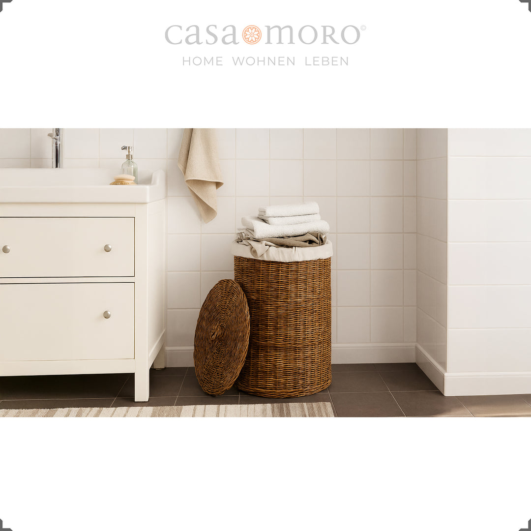Dunkelbrauner Rattan-Wäschekorb mit Deckel und Innenbeutel im hellen Badezimmerambiente, dekoriert mit Handtüchern