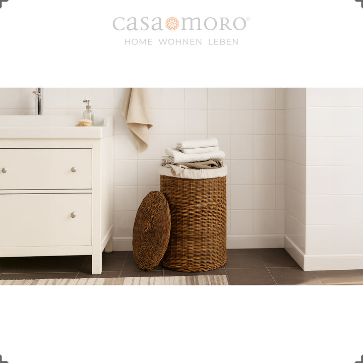 Dunkelbrauner Rattan-Wäschekorb mit Deckel und Innenbeutel im hellen Badezimmerambiente, dekoriert mit Handtüchern